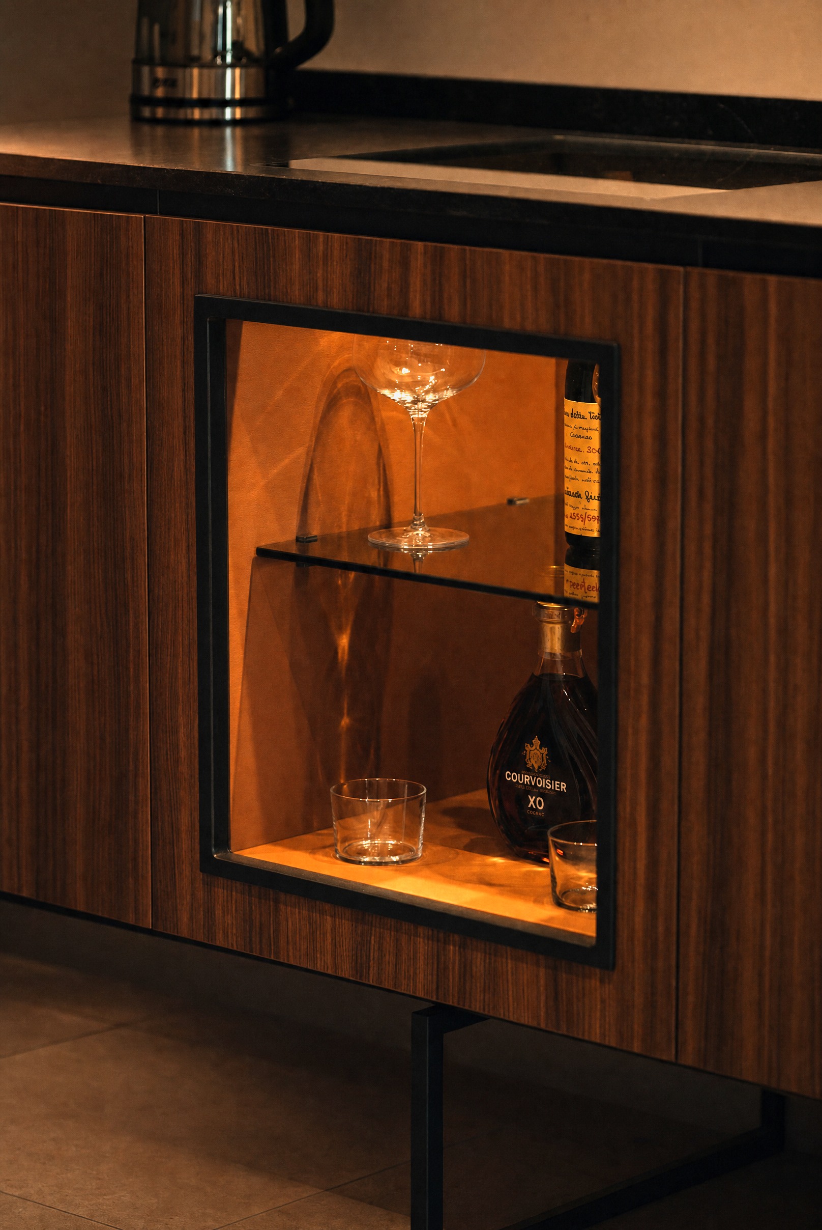 Backlit in-room bar niche with a cognac decanter and coupe glasses
